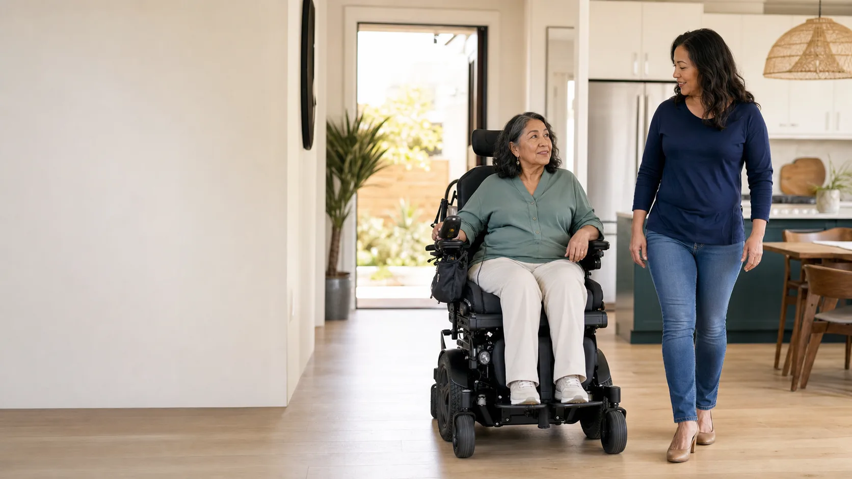 A woman using a custom power wheelchair moving through her home beside her adult daughter